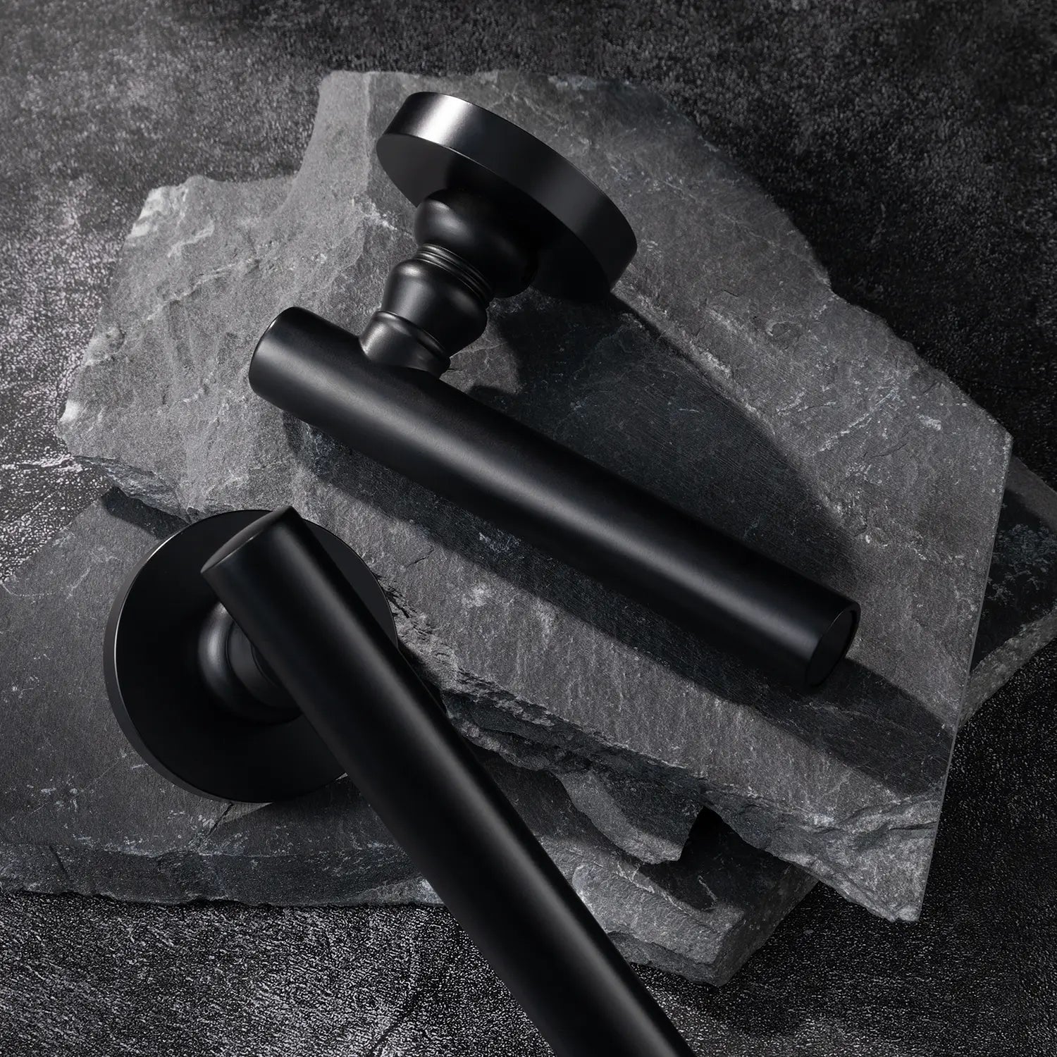 Two Alda door handles in black finish, displayed on a textured stone background.