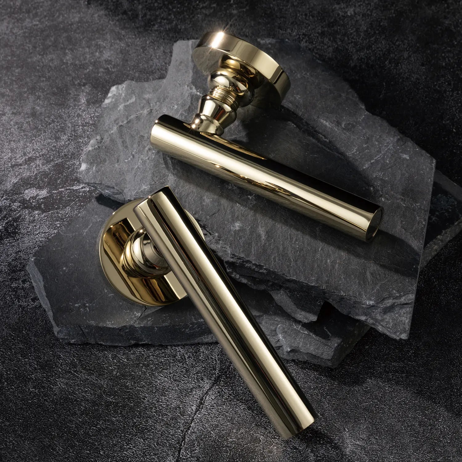 Two Alda door handles in polished brass finish, displayed on a textured stone background.