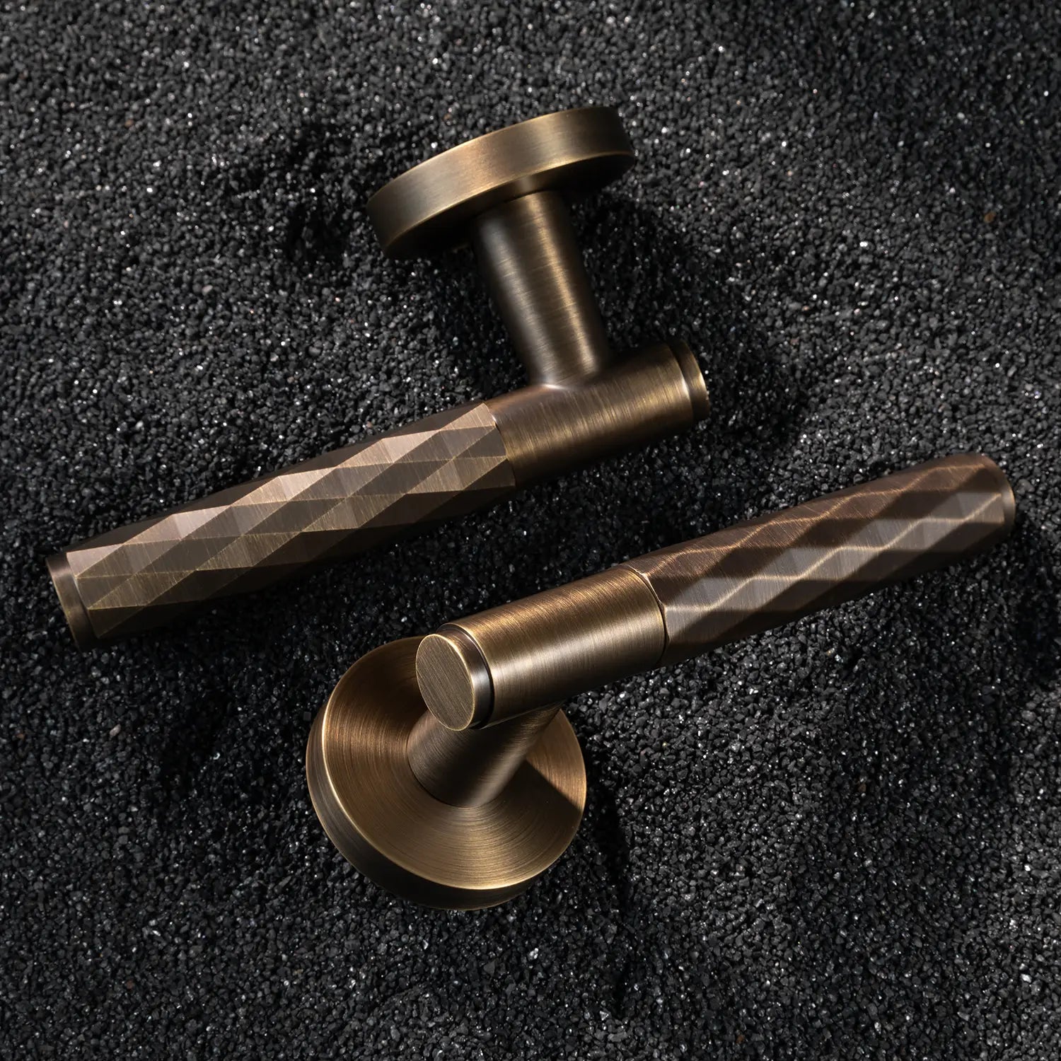 Two Fendal-01 internal door handles in antique brass finish with diamond pattern grip, displayed on a textured stone background.