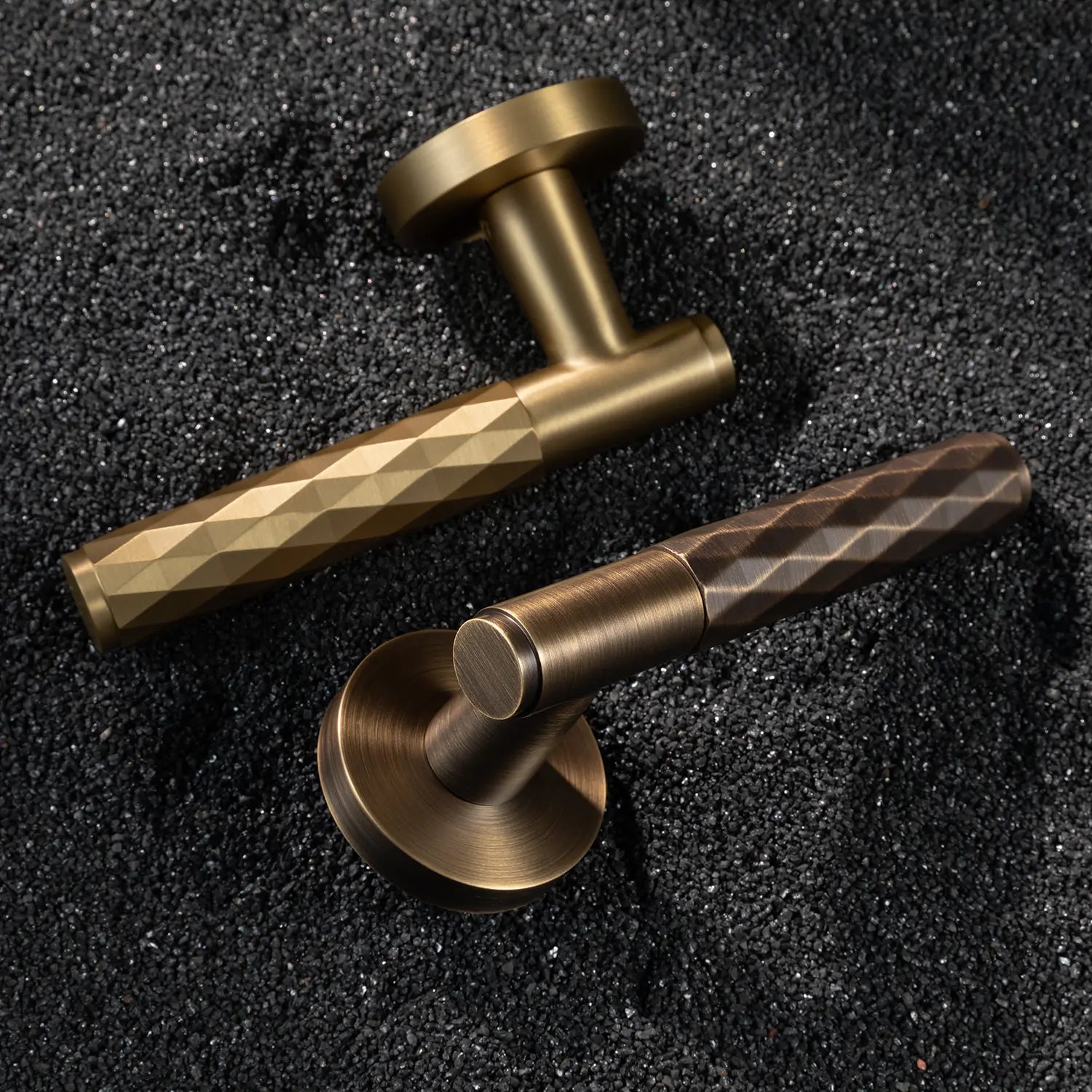Two Fendal-01 door handles in satin brass and antique brass finishes with diamond pattern grips, displayed on a textured stone background.