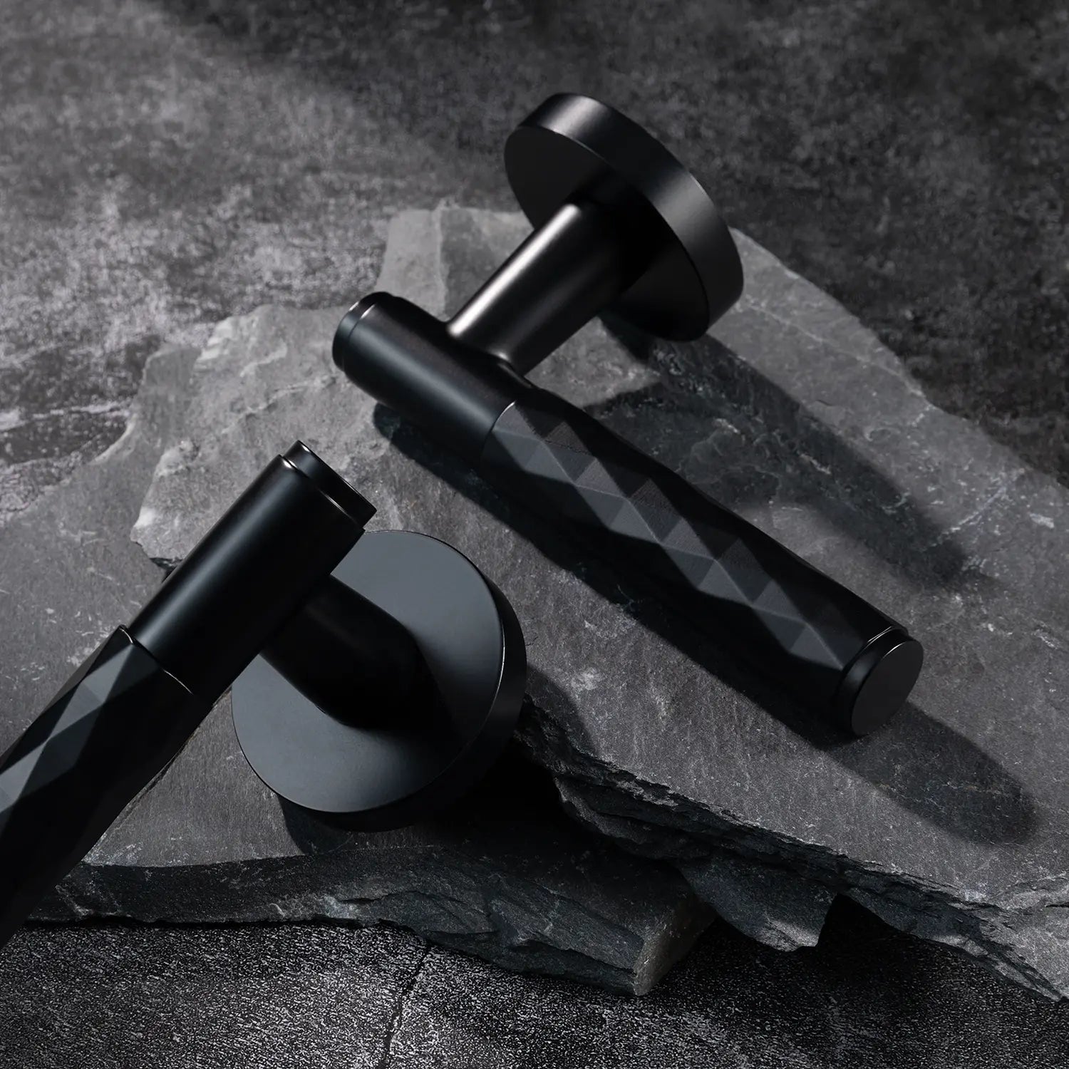 Two Fendal-01 internal door handles in black finish with diamond pattern grip, displayed on a textured stone background.