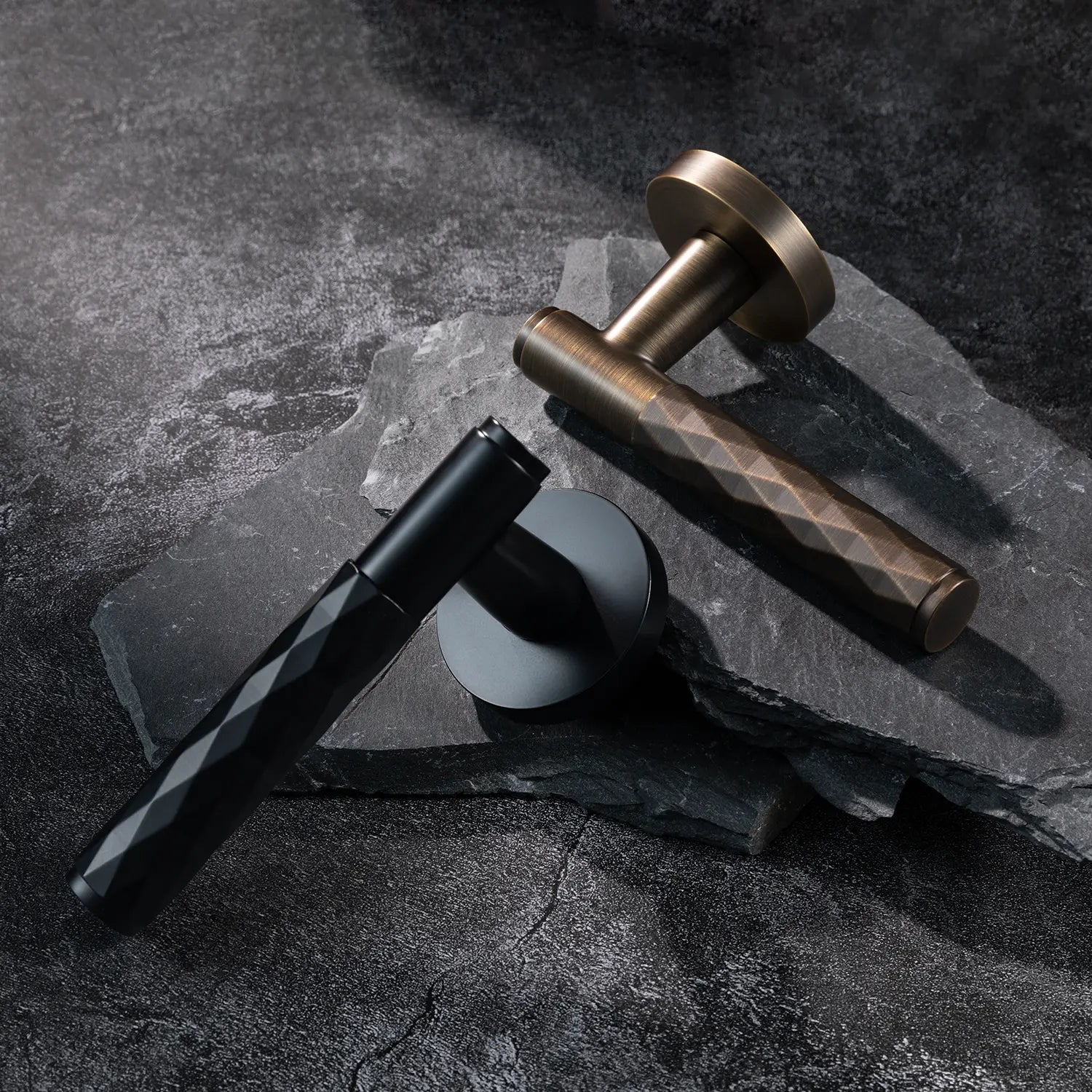 Two Fendal-01 door handles in antique brass and black finishes with diamond pattern grips, displayed on a textured stone background.