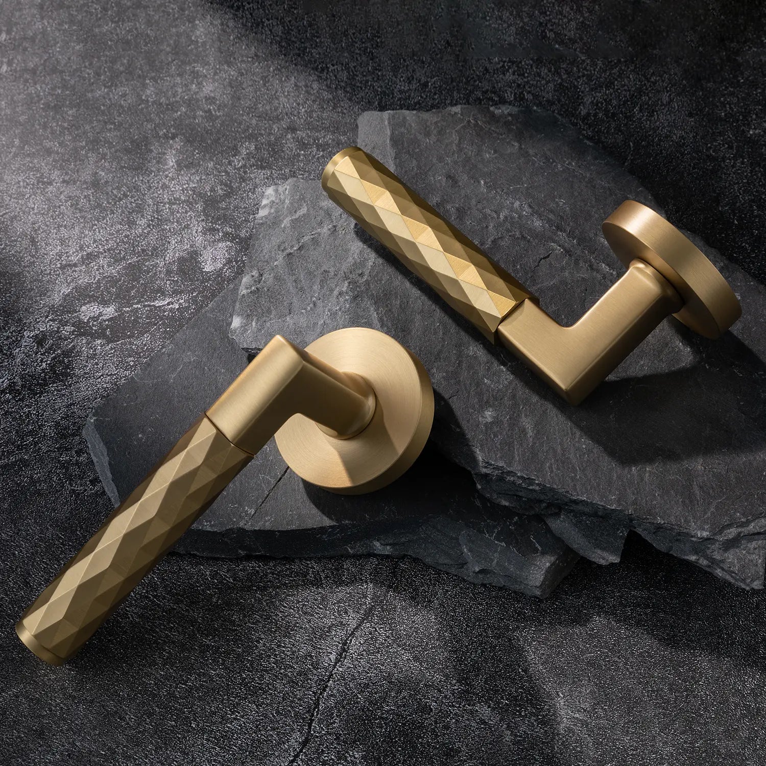 Two Fendal-02 satin brass internal door handles with diamond pattern grip, showcased on a textured stone background.