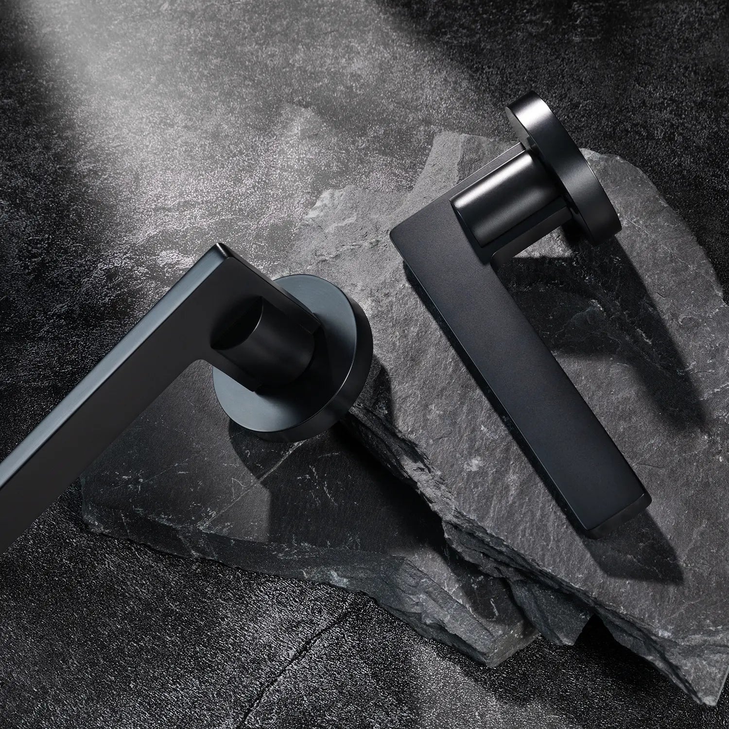 Two Filda door handles in black finish, displayed on a textured stone background.