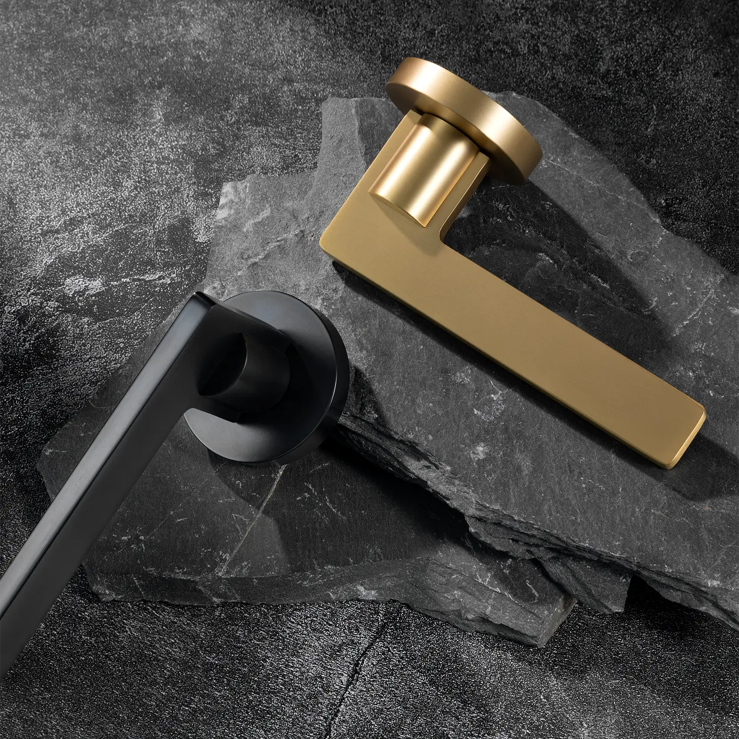 Two Filda door handles in satin brass and black finishes, displayed together on a textured stone background.