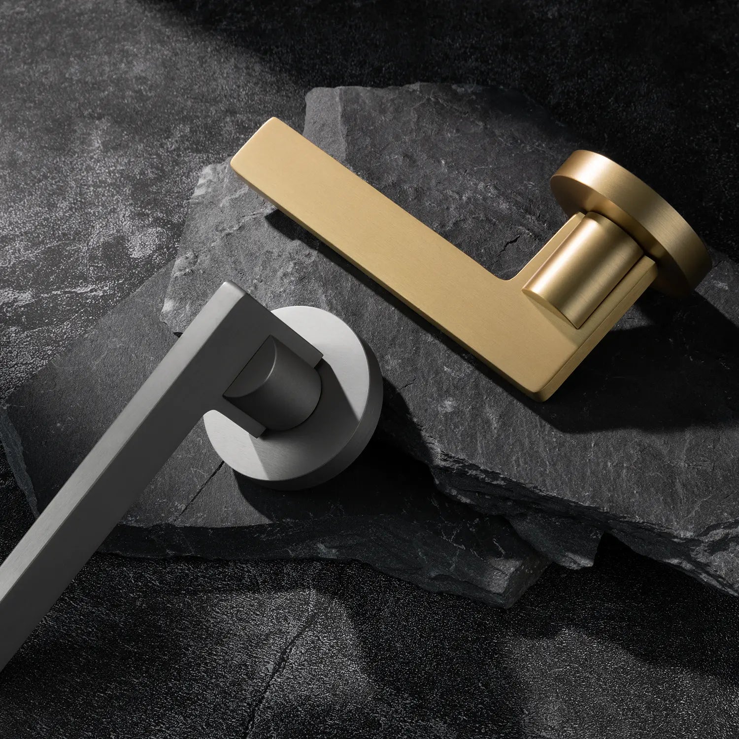 Two Filda door handles in satin brass and nickel finishes, displayed together on a textured stone background.