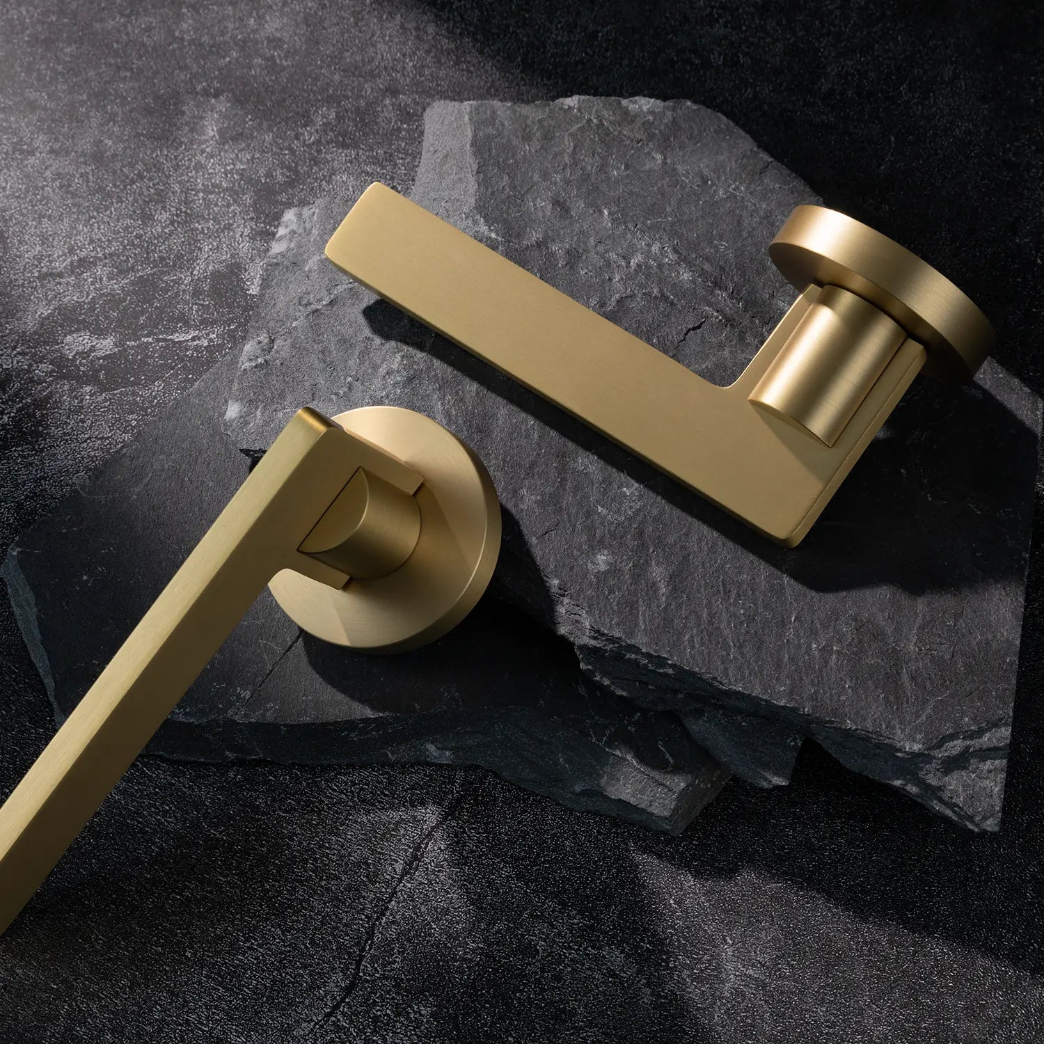 Two Filda door handles in satin brass finish, displayed on a textured stone background.