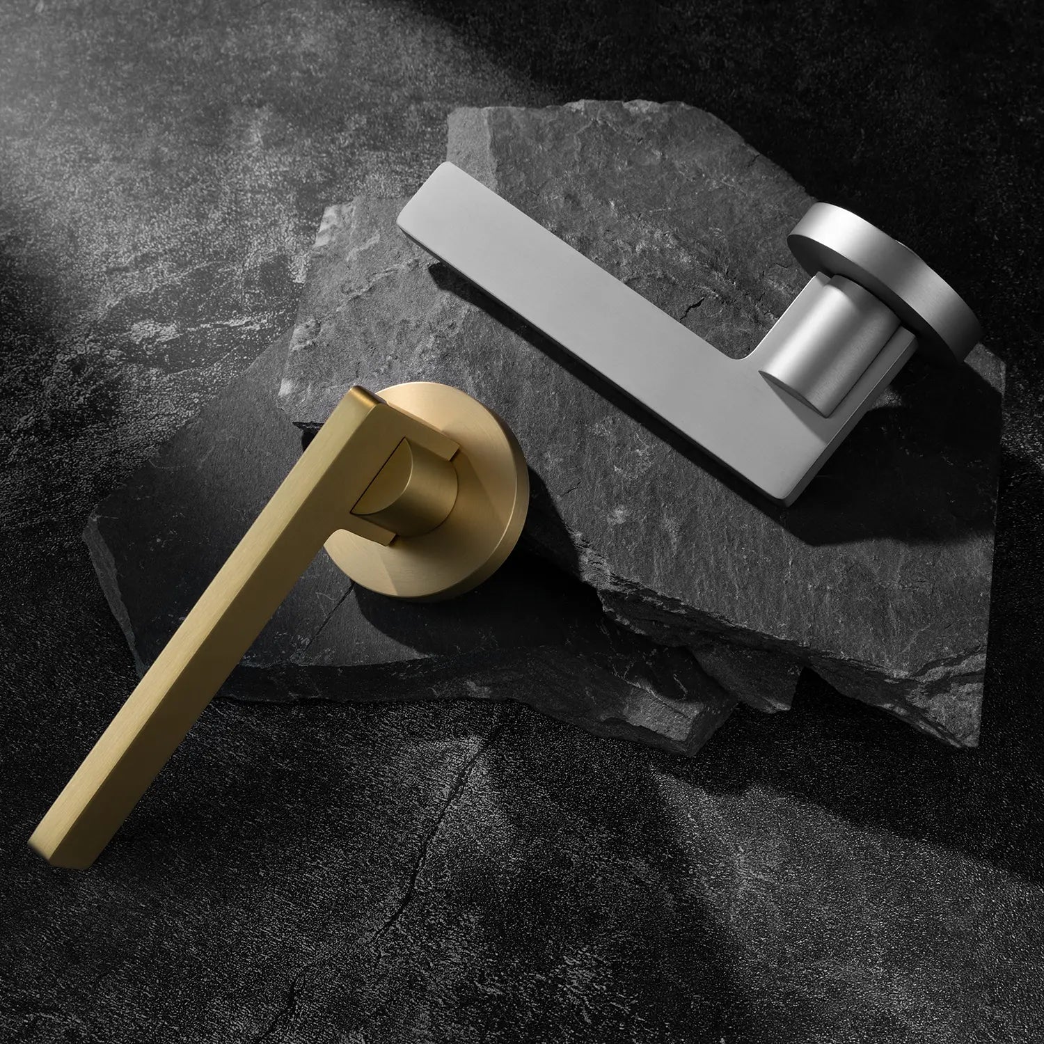 Two Filda door handles in satin brass and nickel finishes, displayed together on a textured stone background.