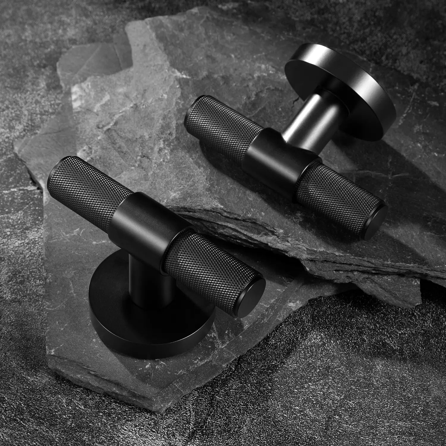 Heik internal door handles in matte black finish, one standing upright and another angled on round rose bases, positioned on layered stone slabs with a textured surface.