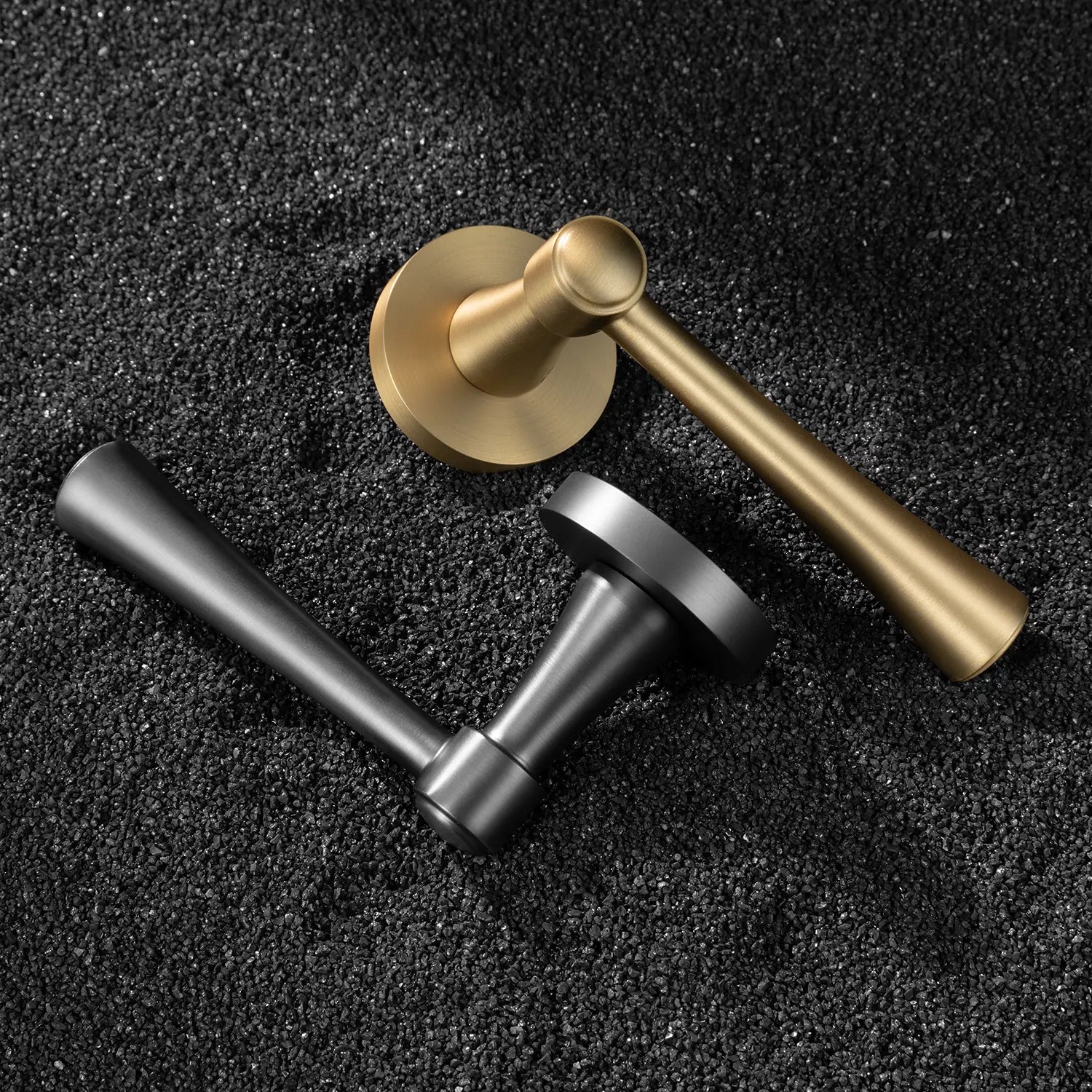 Two Hilda door handles in satin brass and charcoal grey finishes, elegantly positioned on a textured black surface. Featuring sleek and timeless cone-shaped design for modern interiors.