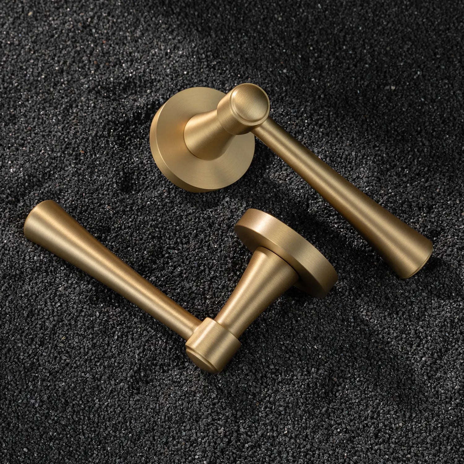 Two Hilda door handles in satin brass finish, elegantly positioned on a textured black surface. Featuring sleek and timeless cone-shaped design for modern interiors.