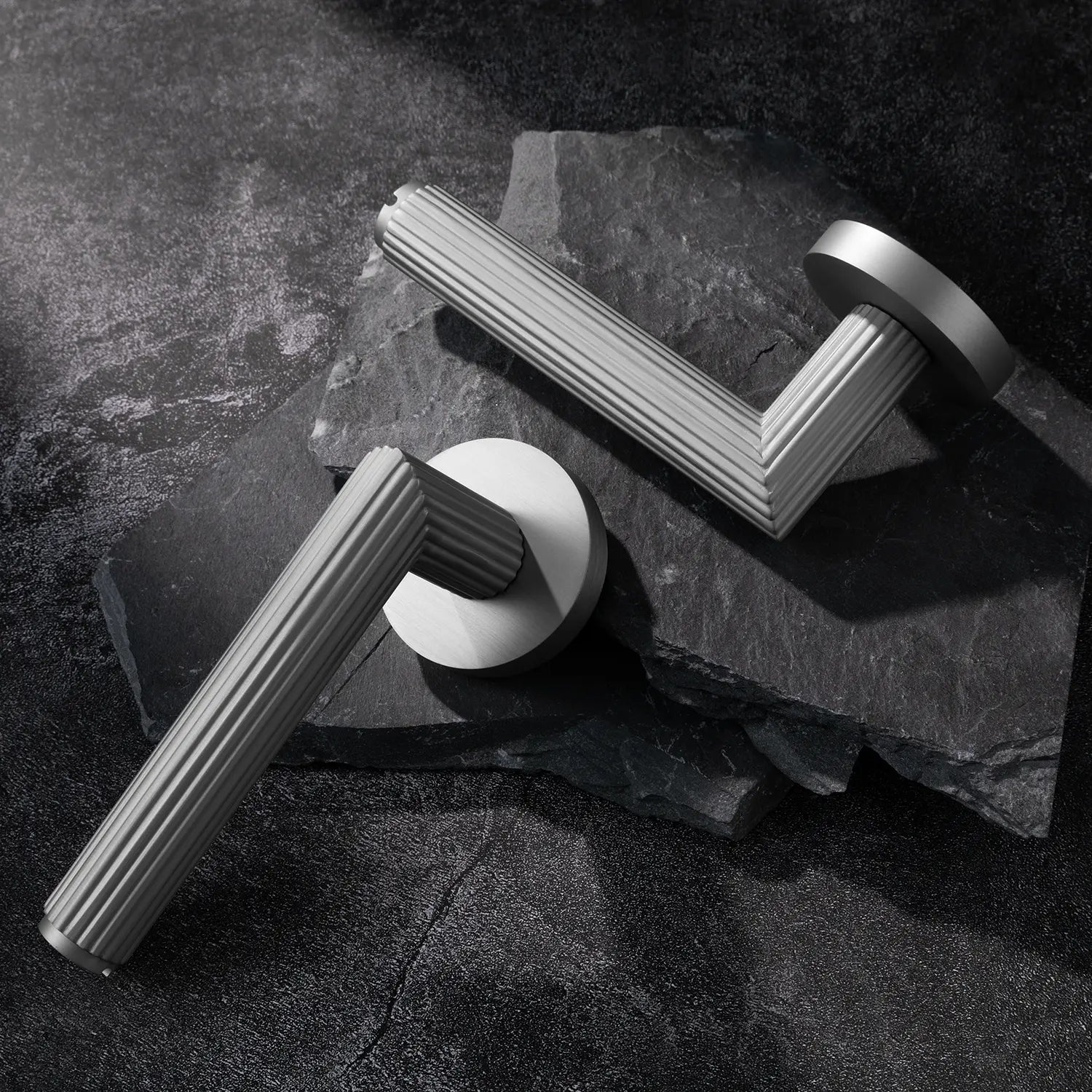 Two Midal door handles in nickel finish, displayed diagonally on a textured stone surface, featuring a bold linear pattern for a contemporary aesthetic.
