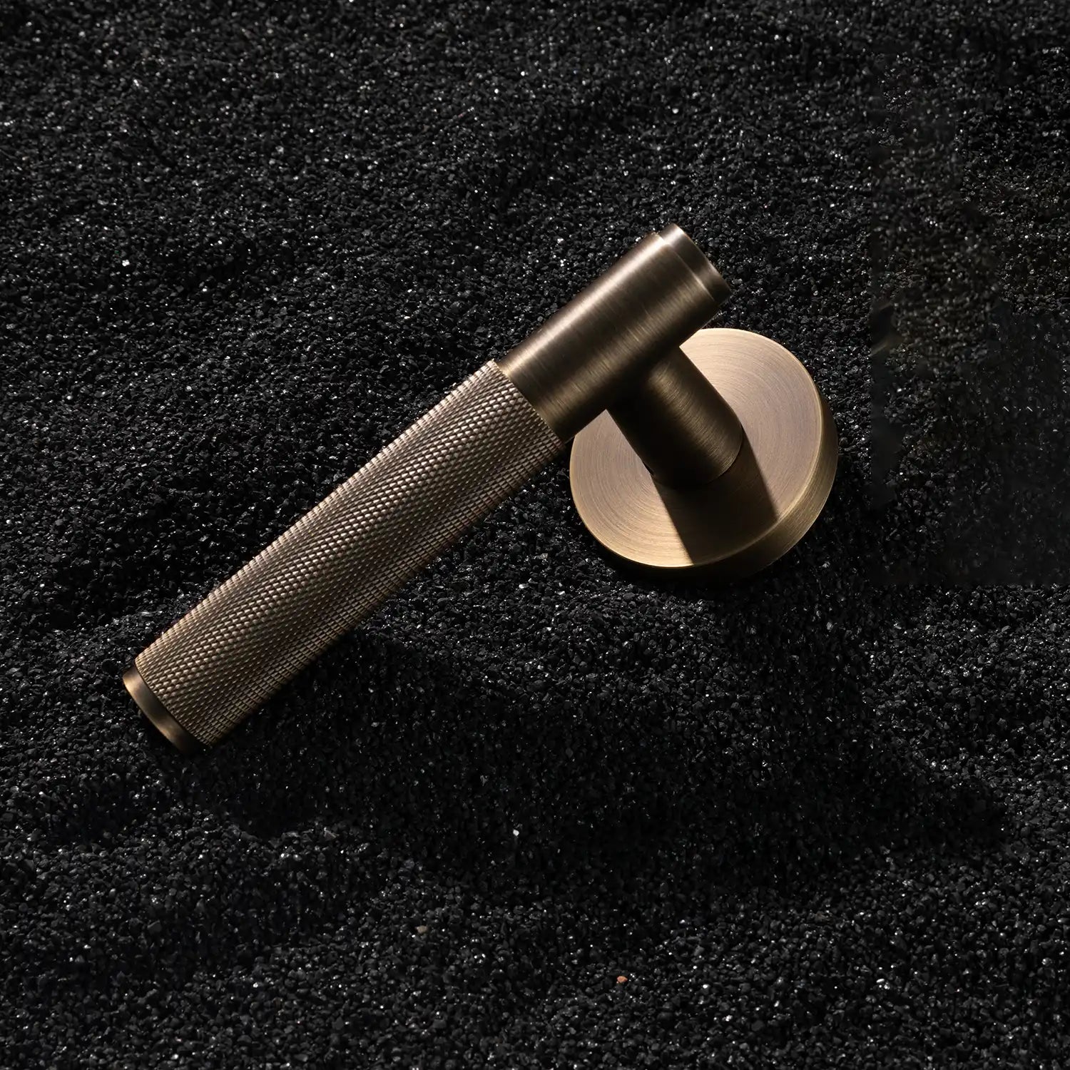 Svik-01 internal door handle with knurled pattern in antique brass finish, displayed vertically on a textured gravel background.