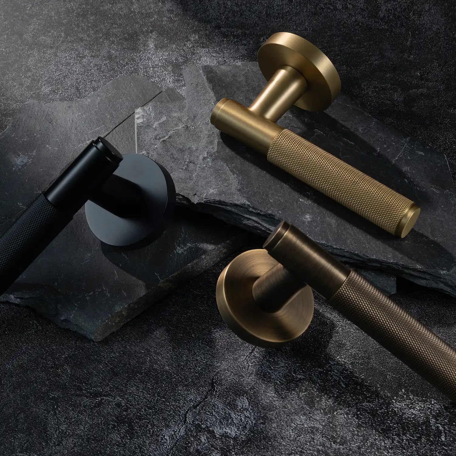 Three Svik-01 internal door handles with knurled pattern, featuring black, satin brass and antique brass finishes, displayed on layered slate stone background.