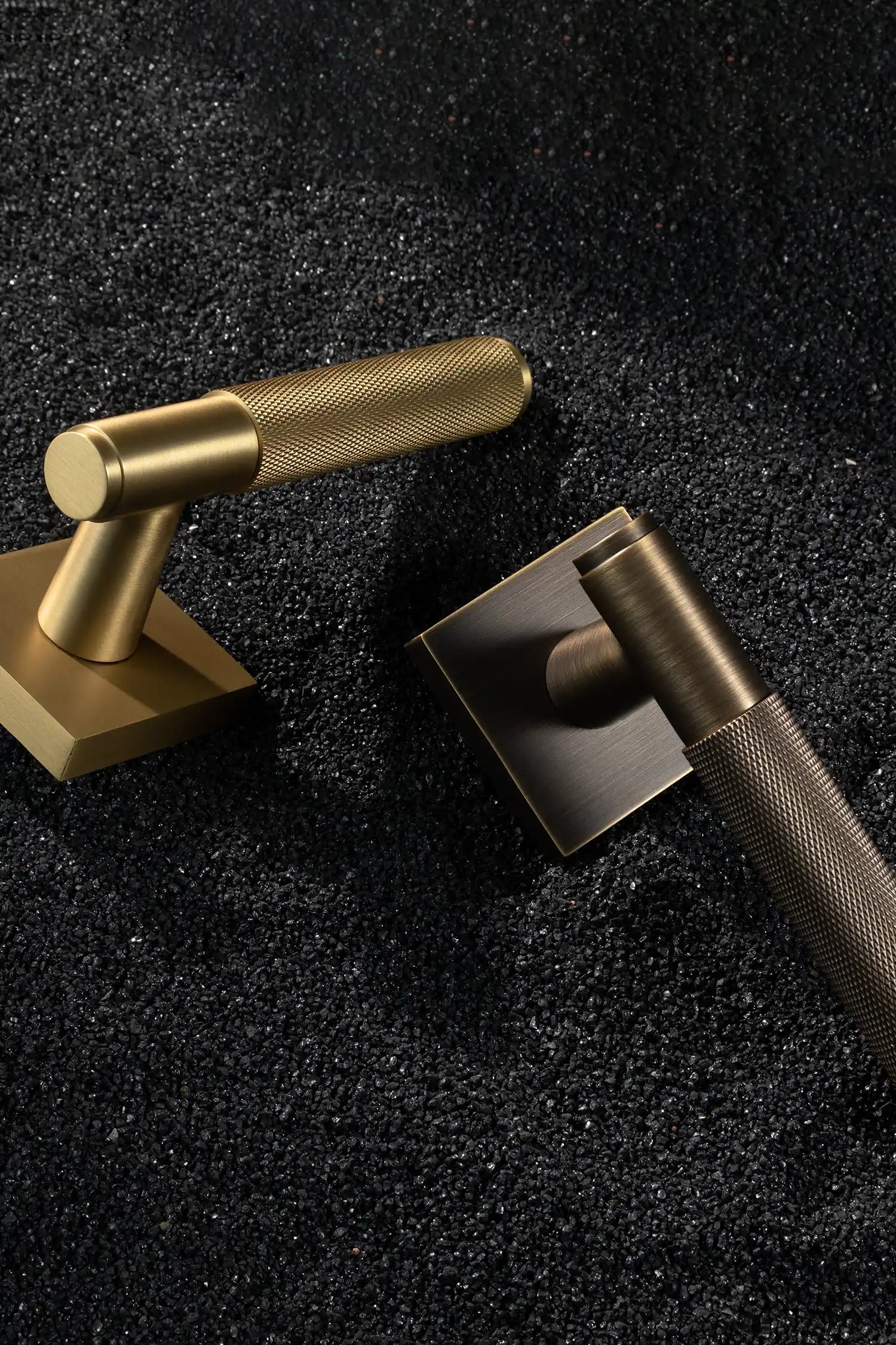 Svik-01 internal door handles in satin brass and antique brass finishes, featuring knurled pattern grips, paired with square rose bases, displayed on a textured black gravel background.