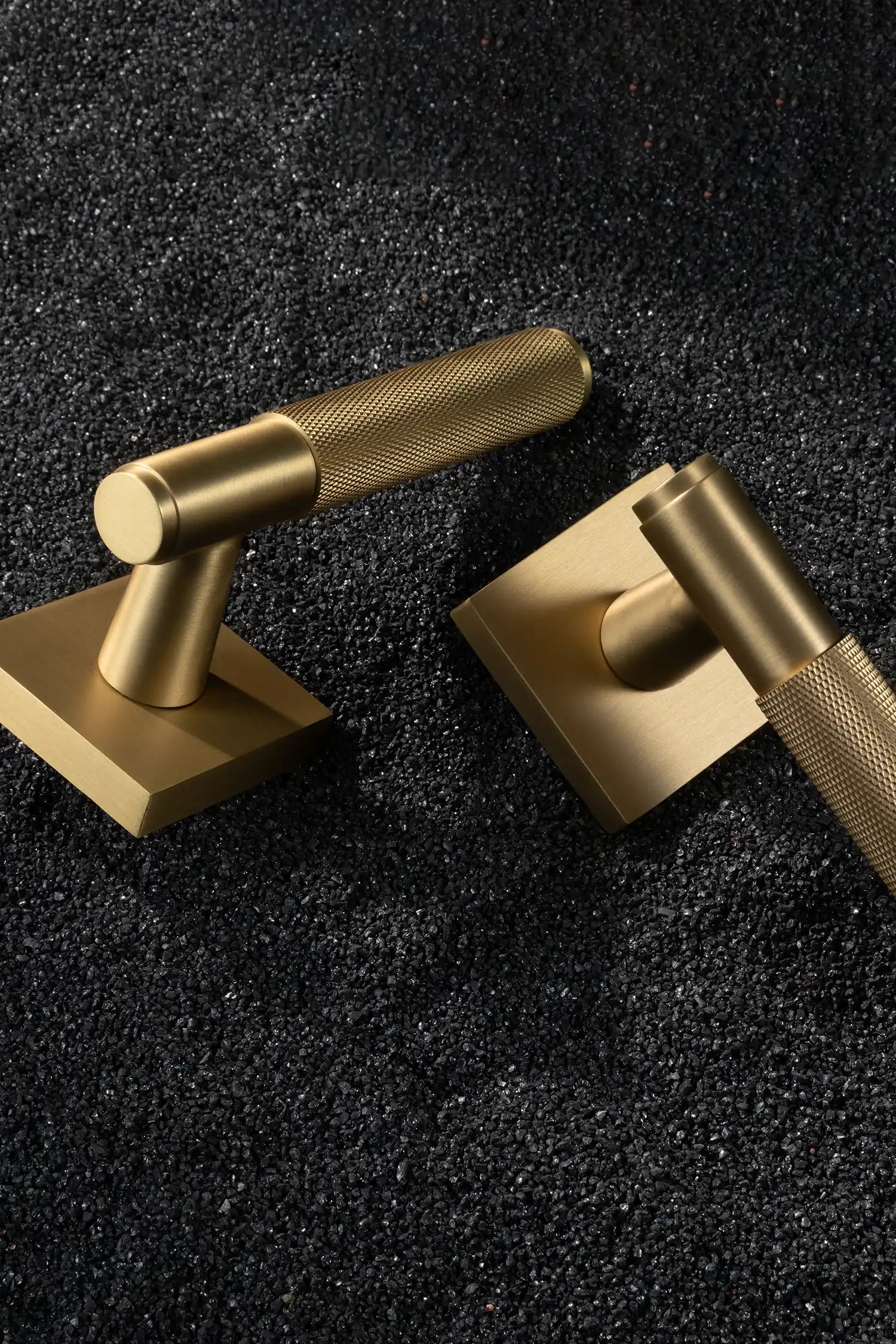 Svik-01 internal door handles in satin brass finish, featuring knurled pattern grips, paired with square rose bases, displayed on a textured black gravel background.