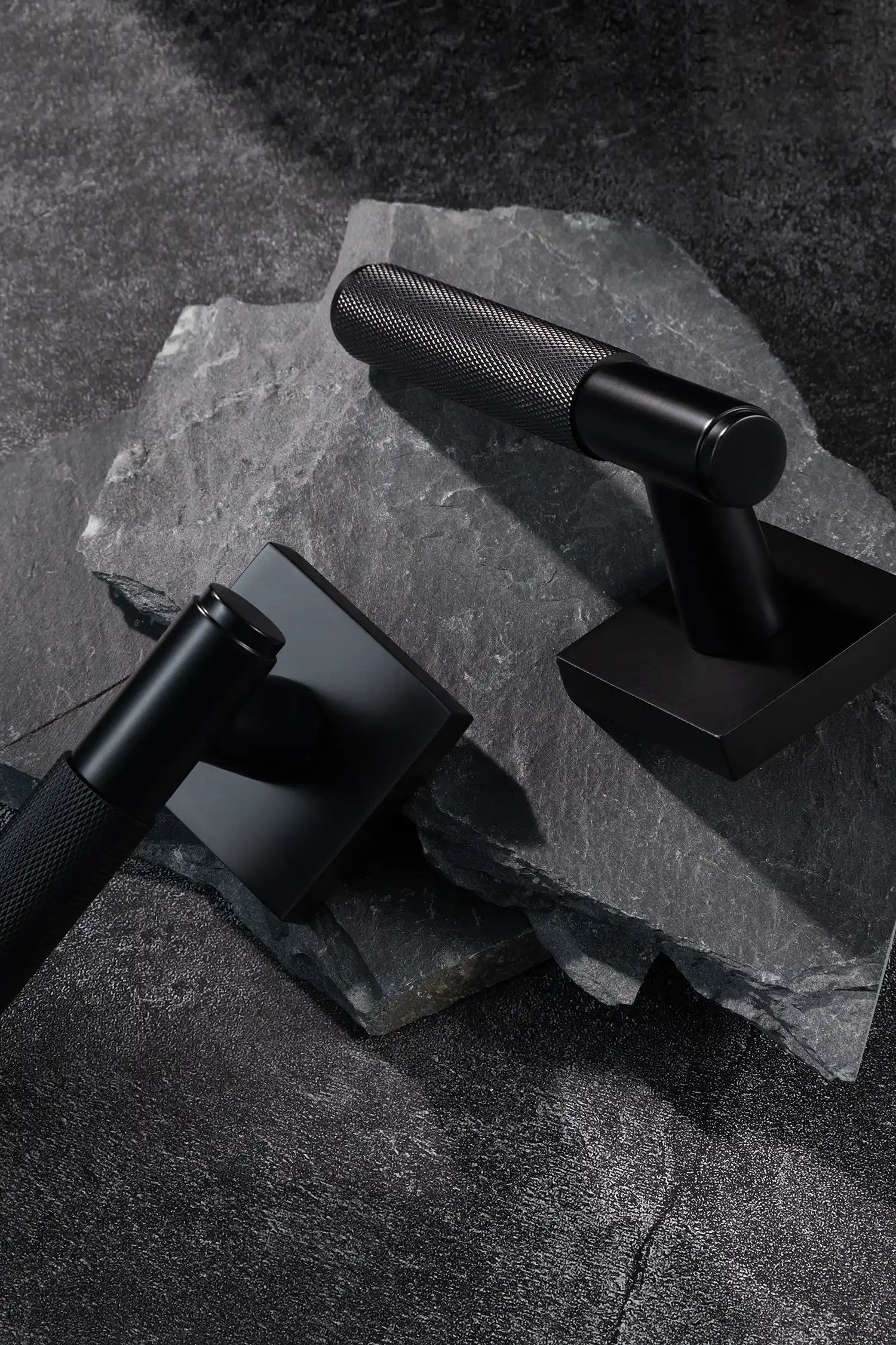 Svik-01 internal door handles in black finish, featuring knurled pattern grips, paired with square rose bases, displayed on a slate stone surface.