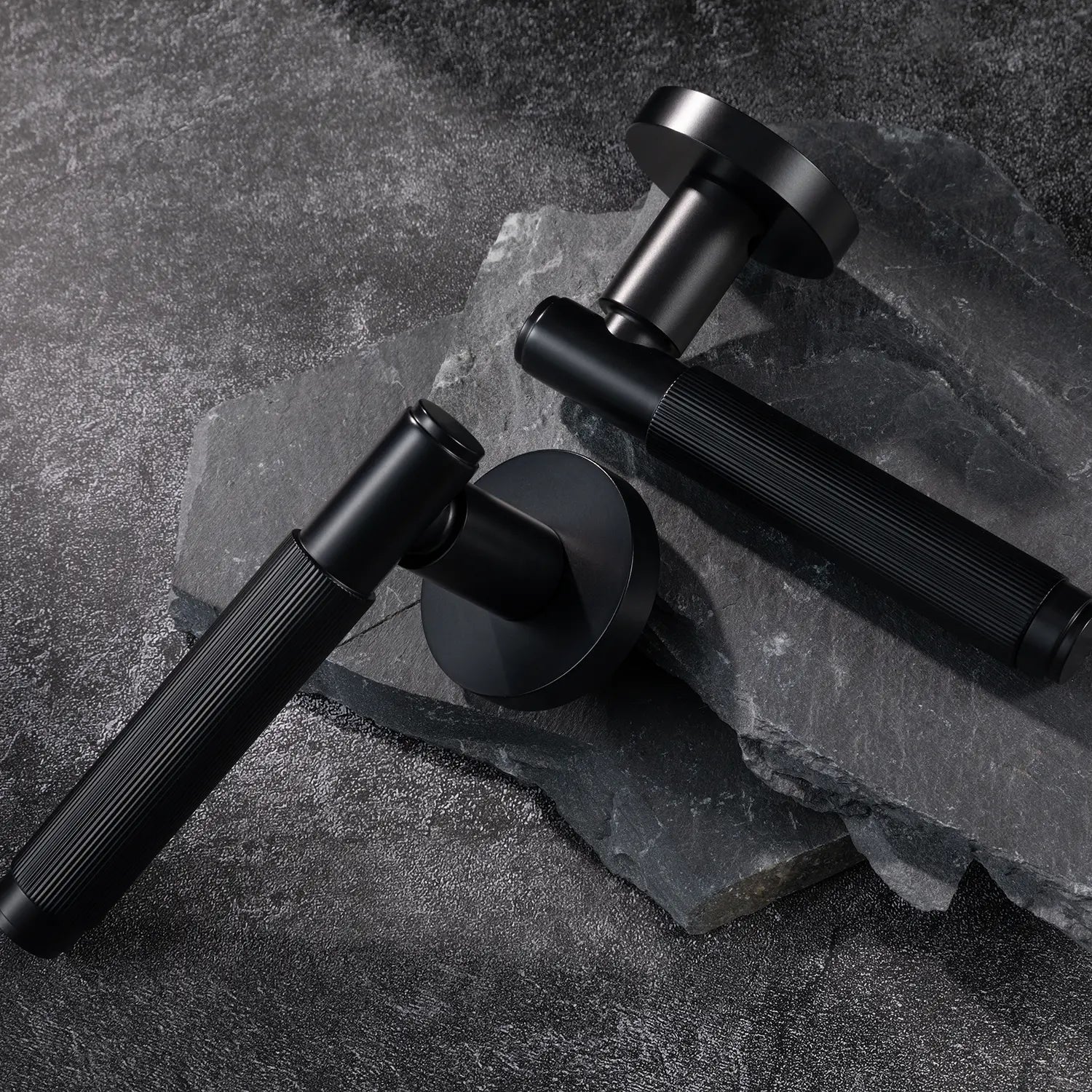 Two Svik-02 internal door handles in black finish, placed on textured stone slabs, showcasing linear pattern design on grip.