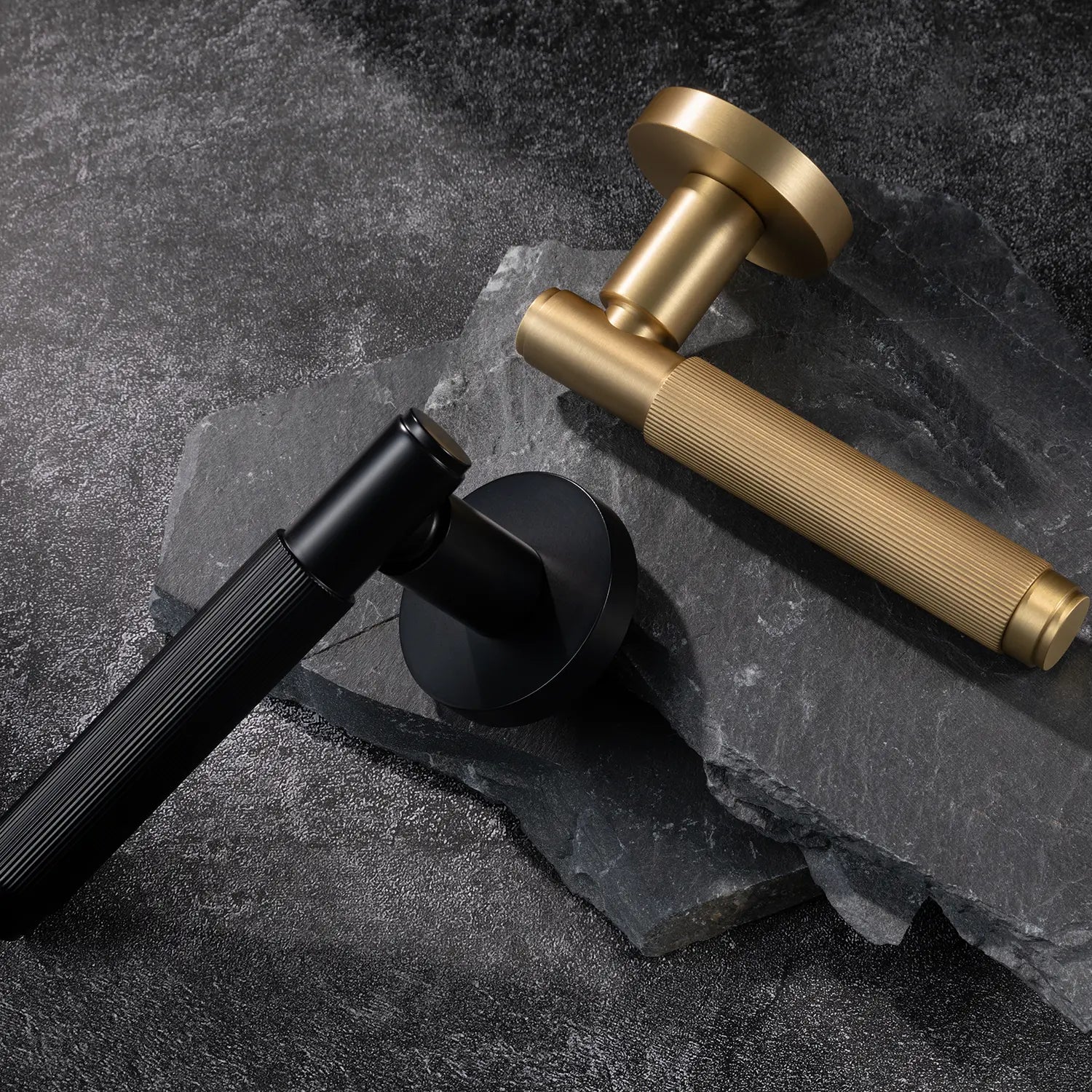 Two Svik-02 internal door handles in satin brass and black finishes, positioned on dark textured stone, highlighting contrasting finishes with linear pattern details.