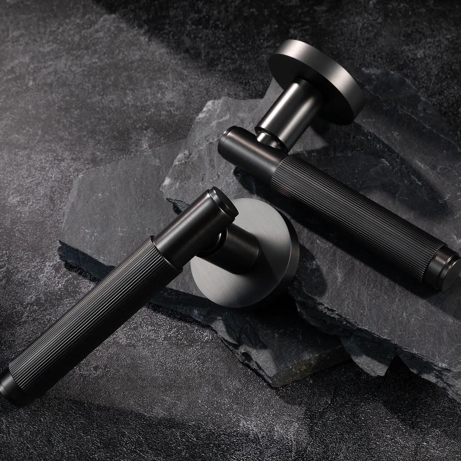 Two Svik-02 internal door handles in charcoal grey finish, placed on textured stone slabs, showcasing linear pattern design on grip.