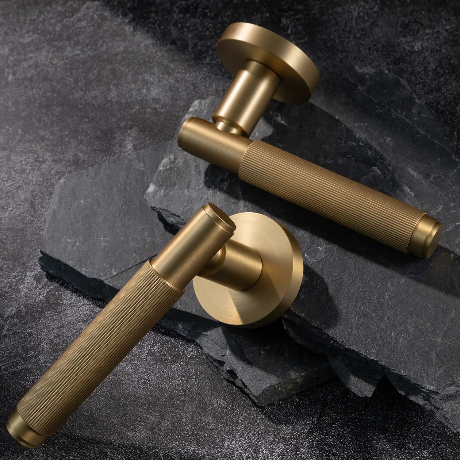 Two Svik-02 internal door handles in satin brass finish, placed on textured stone slabs, showcasing linear pattern design on grip.