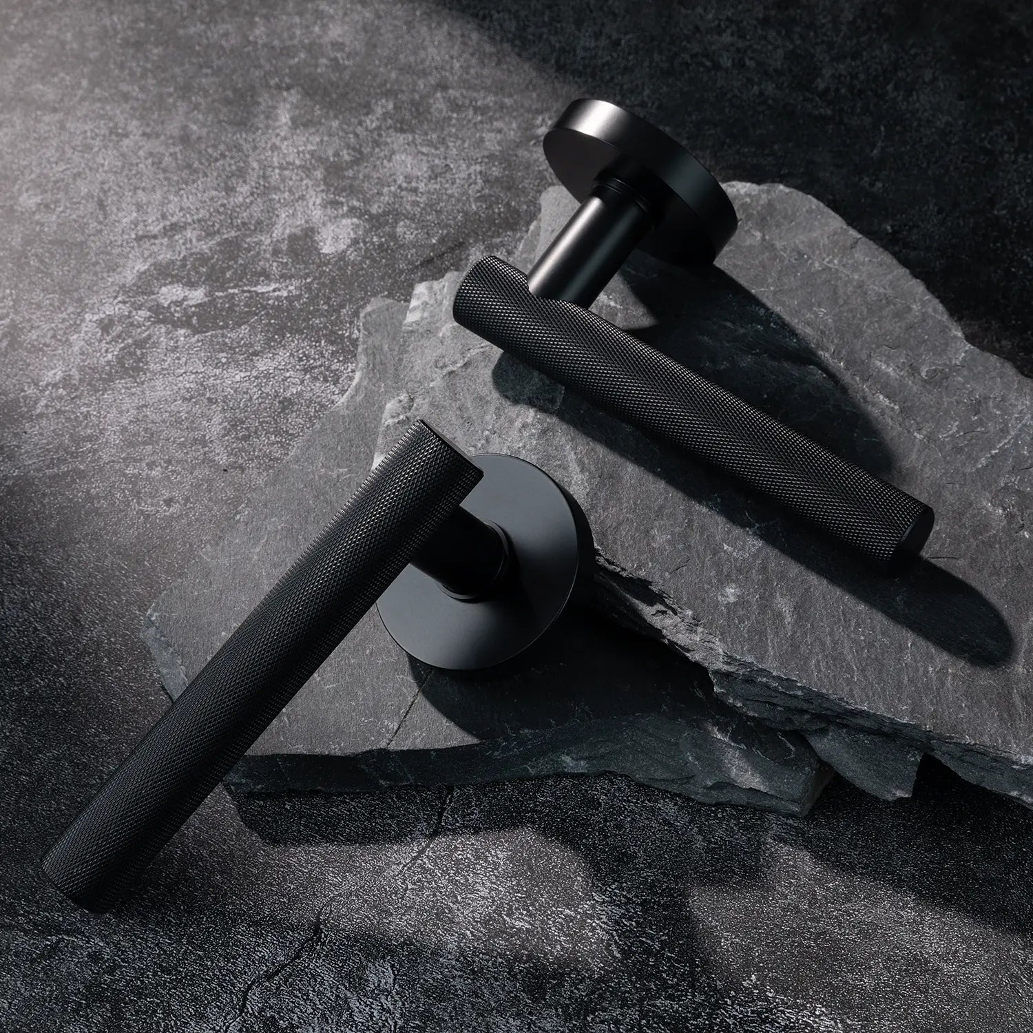 Two Tord-01 internal door handles in black finish, featuring a fully knurled pattern handle design, placed diagonally on stacked stone slabs with a textured background.