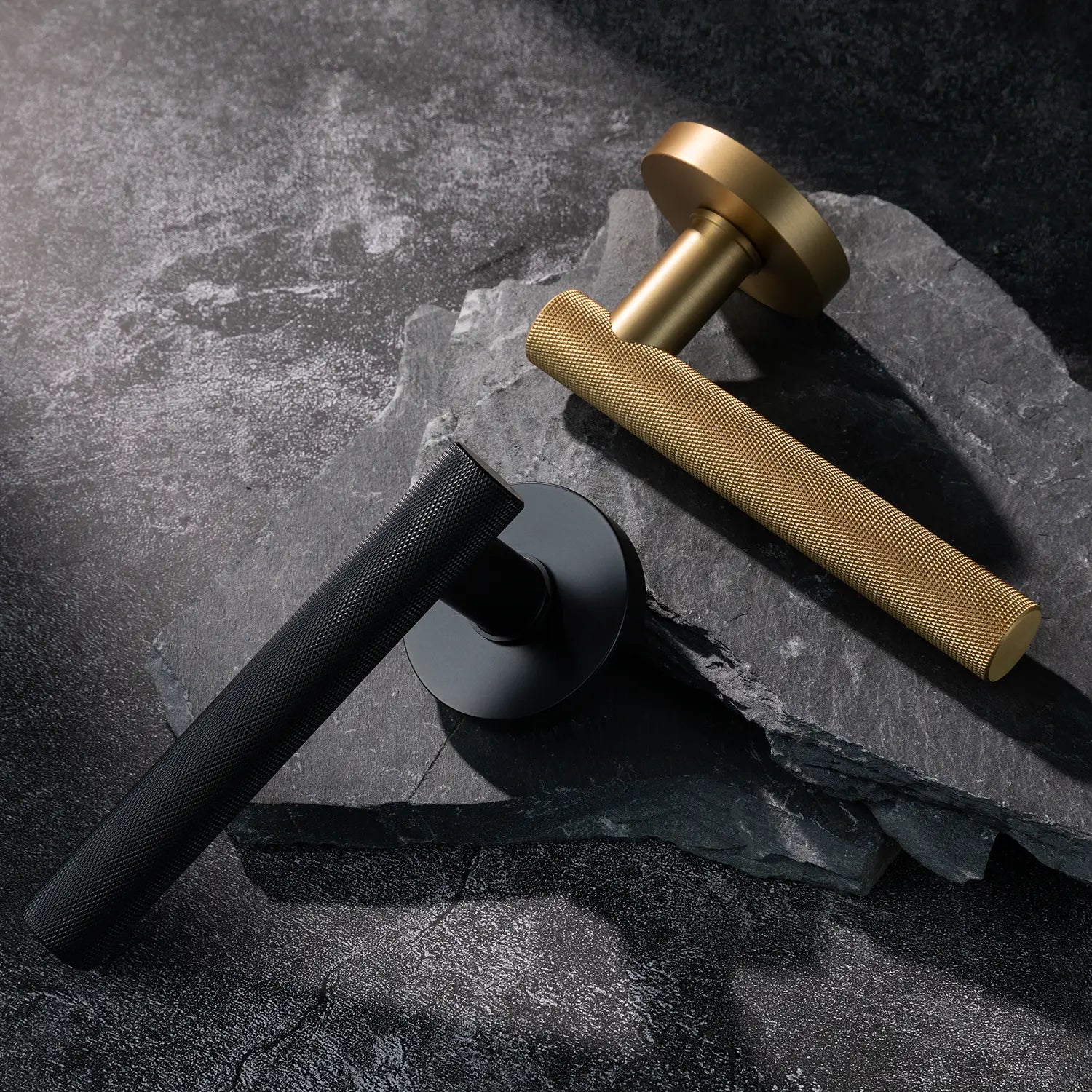 Two Tord-01 internal door handles, one in satin brass and the other in black finish, both featuring a fully knurled pattern handle design, placed diagonally on stacked stone slabs with a textured background.