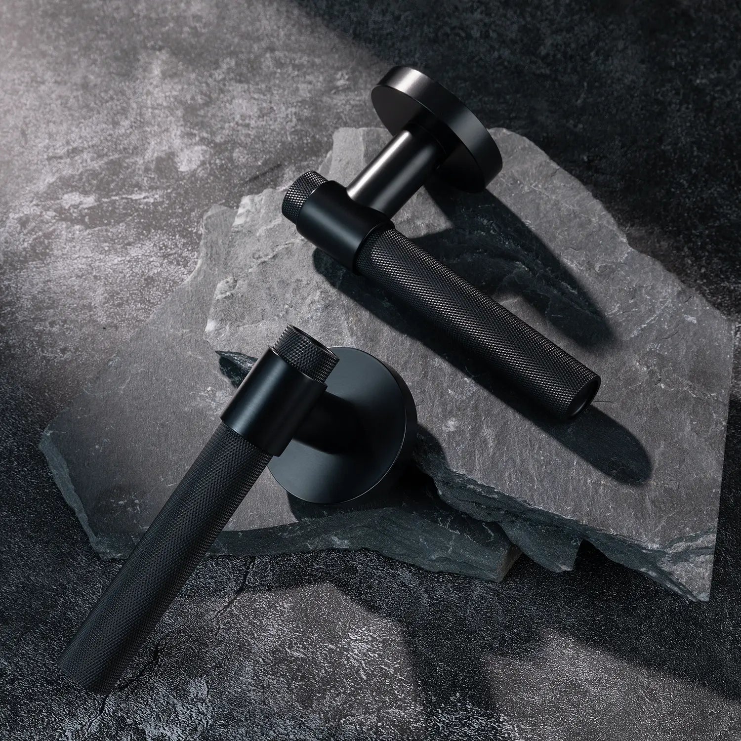 Two Tord-02 internal door handles in black finish, featuring a large area of knurled pattern on the grip, positioned on overlapping dark stone slabs.