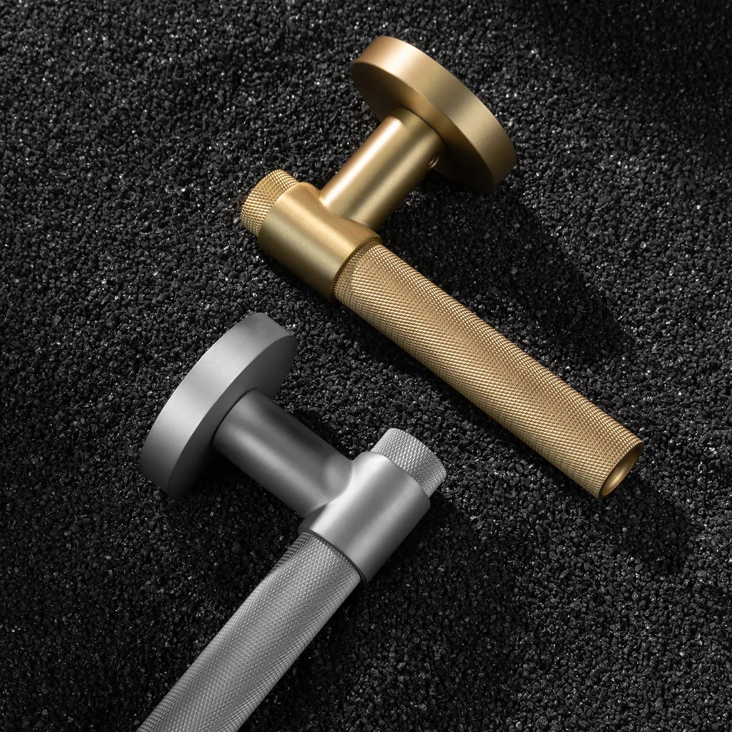 Two Tord-02 internal door handles in satin brass and nickel finishes, featuring a large area of knurled pattern on the grip, displayed on a textured gravel background.