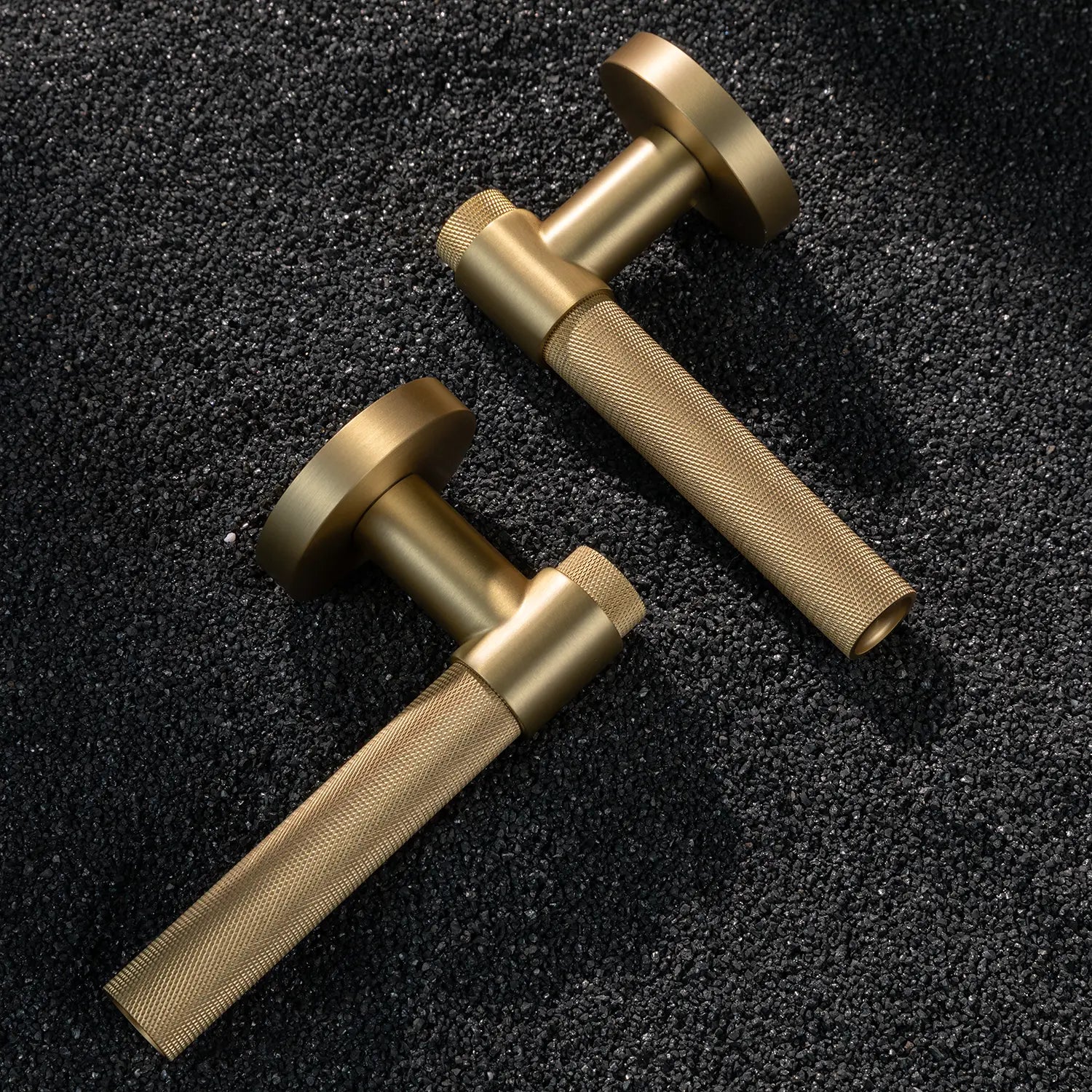 Two Tord-02 internal door handles in satin brass finish, featuring a large area of knurled pattern on the grip, displayed on a textured gravel background.