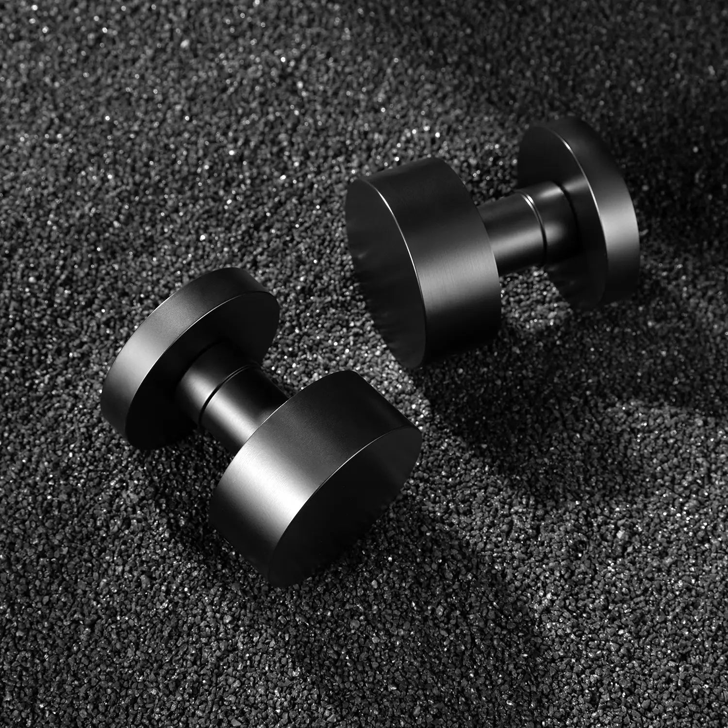 Two Solda door knobs in black finish, displayed on a textured black gravel background.