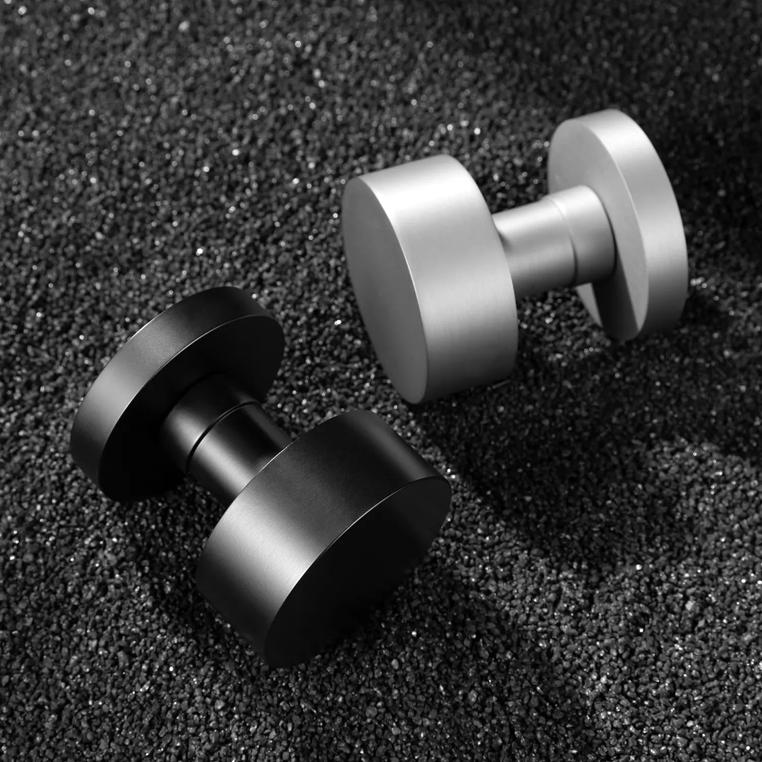 Two Solda door knobs in black and nickel finishes, showcased on a textured black gravel surface.