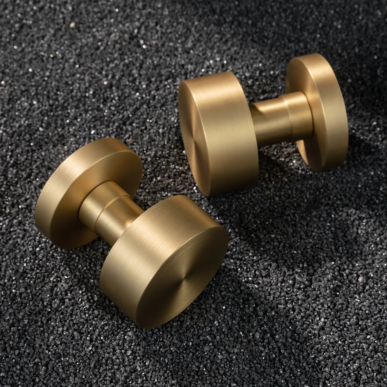 Two Solda door knobs in satin brass finish, displayed on a textured black gravel background.