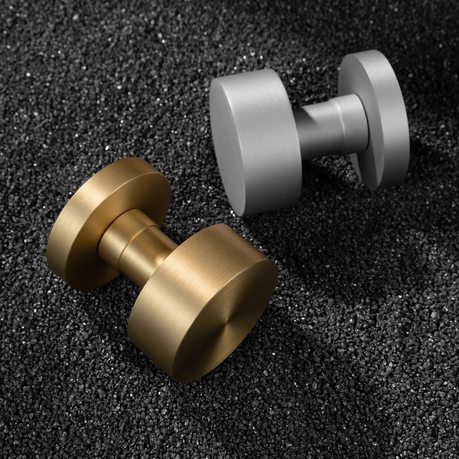 Two Solda door knobs in satin brass and nickel finishes, showcased on a textured black gravel surface.
