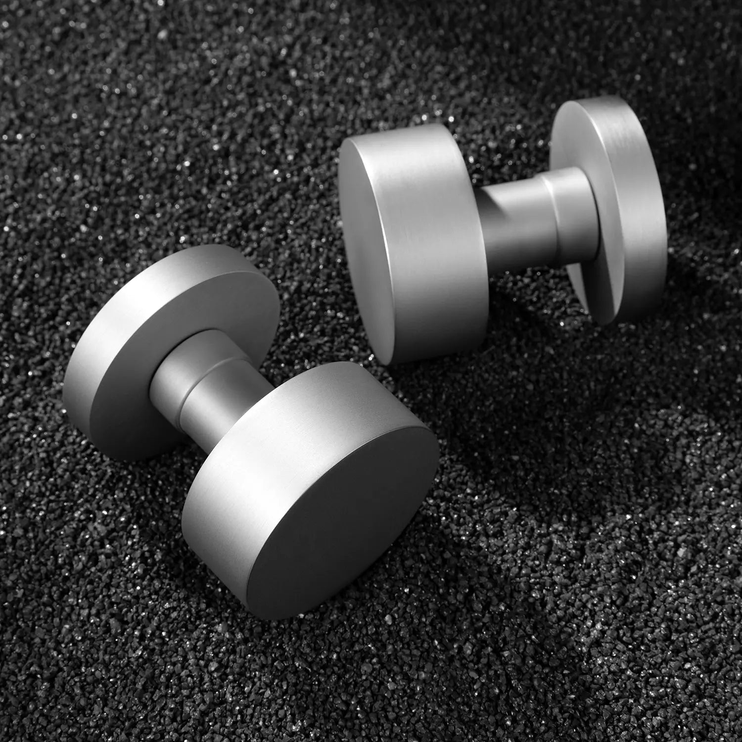 Two Solda door knobs in nickel finish, displayed on a textured black gravel background, emphasizing their sleek cylindrical design and modern aesthetic.