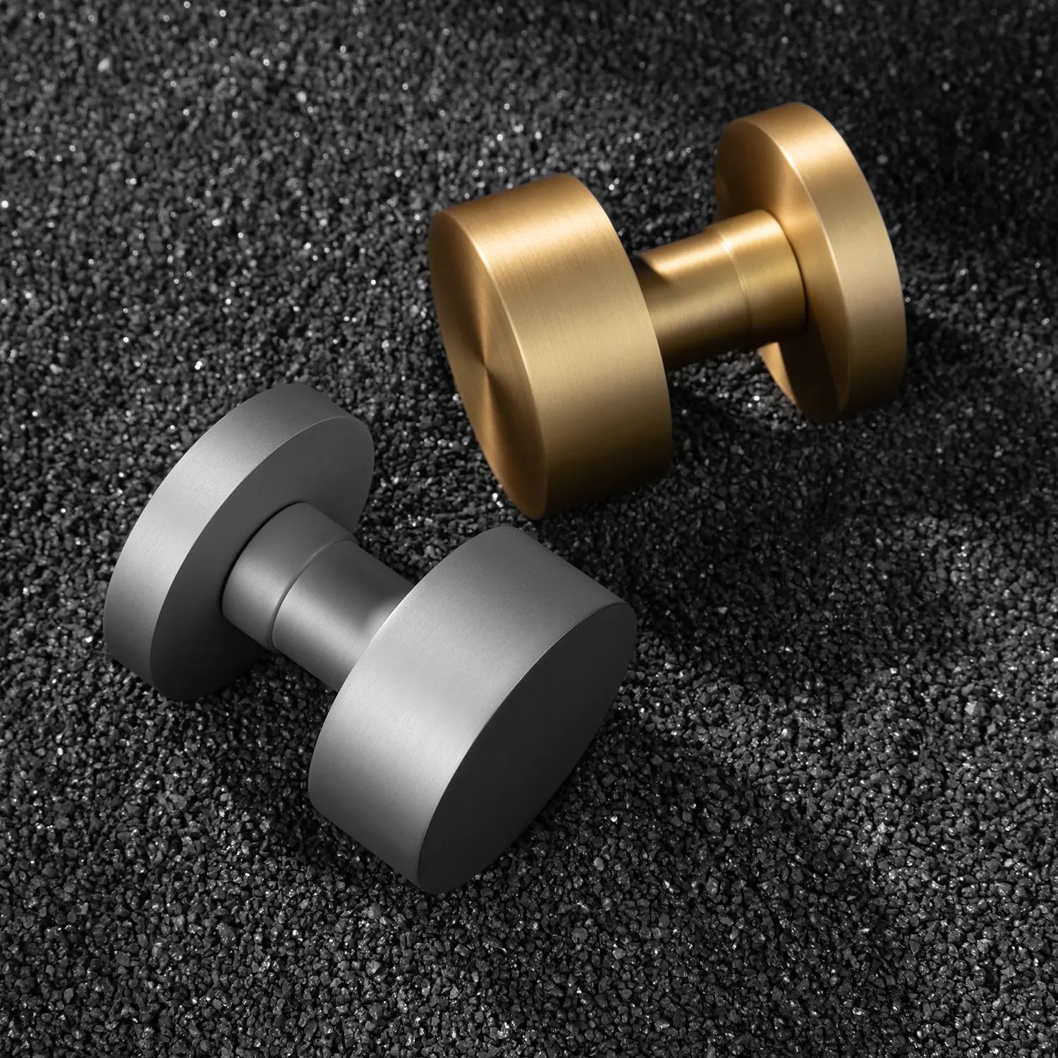 Two Solda door knobs in satin brass and nickel finishes, showcased on a textured black gravel surface.